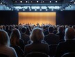 © Karn AS Images - The rear view of a diverse audience attentively listening to a speaker at a business conference, with a well-lit stage and professional setting