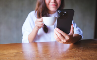 Canvas Print - Closeup image of a young woman holding and using mobile phone while drinking coffee in cafe