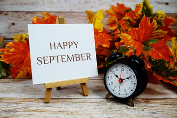 Canvas Print - Happy September text with alarm clock and maple leaf decoration on wooden background