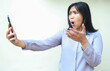 © M Alfan Setyawan - pretty asian young business woman shocked looking mobile phone hold on hands raising palm, questioning gesture, wearing formal shirt standing over isolated white background