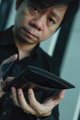 Poster - A man is holding a wallet with a hole in it. He looks sad and disappointed. The wallet is black and has a zipper