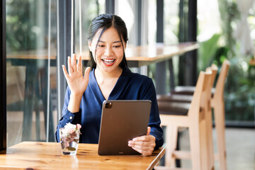 Wall Mural - beautiful asian businesswoman in the cafe, video call with her colleagues via digital tablet and smi
