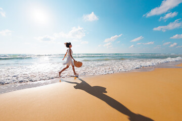 happy girl in a white dress runs along the beach and enjoys her vacation. A carefree girl walks along the beach on a sunny day.