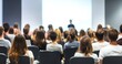 © 为轩 张 - Audience view from behind in a conference room with a white wall, watching a speaker and presentation screen. Scandinavian design style with varied colored attire and some attendees sitting back