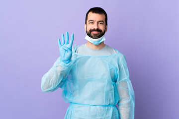 Wall Mural - Surgeon man with beard with blue uniform over isolated purple background happy and counting four with fingers