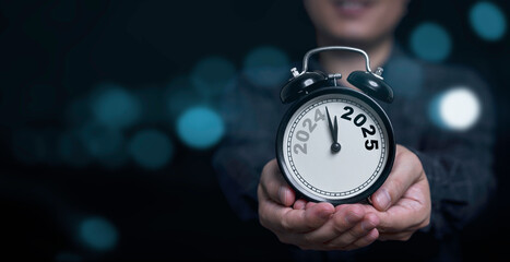 Wall Mural - businessman holding 2024 and 2025 on black alarm clock with copy space for preparation of merry chri