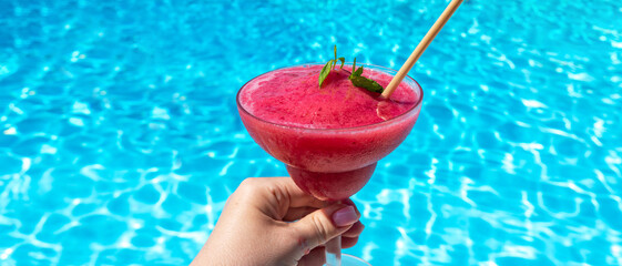 Chilled raspberry or strawberry Daiquiri with mint in hand by pool on sunny day. Concept of summer fun and refreshing drinks