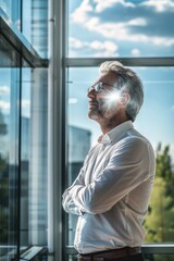 Poster - A man in a white shirt is looking out the window with his arms crossed. He is deep in thought