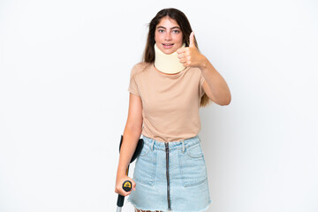 Wall Mural - Young caucasian woman wearing neck brace and crutch isolated on white background with thumbs up because something good has happened