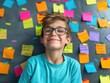 © vefimov - A young boy is smiling and wearing glasses. He is surrounded by colorful sticky notes. Concept of creativity and playfulness