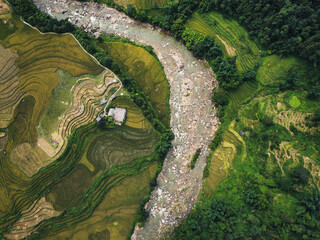 Vertical aerial shot in Sapa, Vietnam of river during rainy season with farmhouses and rice fields at both sides of it