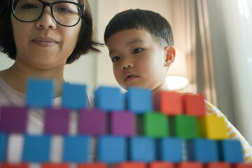 Asian Mother and young son looking at colorful wooden blocks, close-up on faces, educational and bonding activity, indoor setting, focused expressions