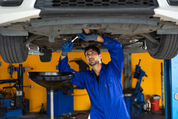 Under car. hispanic latin male mechanic repairs car in garage. Closeup hand. Auto car mechanic checking the oil level of the car engine. Car repair and maintenance