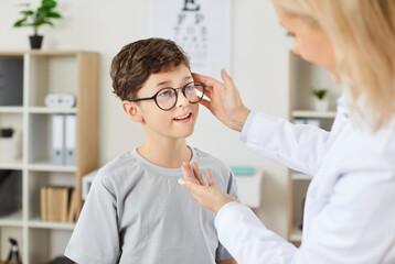 Young female optician doctor looking to her little child patient wearing eyeglasses after eye examination in medical clinic for vision correction. Ophthalmology, eye health concept.