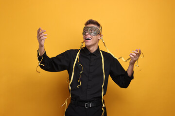 Charming young man wearing carnival mask on orange background