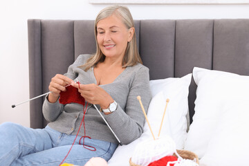 Wall Mural - Smiling senior woman knitting on bed at home