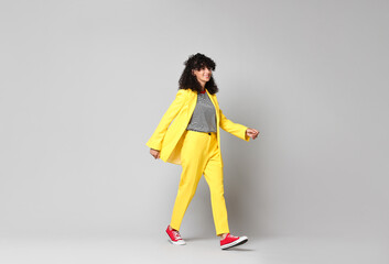 Poster - Beautiful young woman in stylish yellow suit walking on grey background