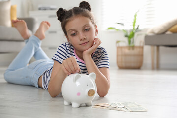 Wall Mural - Pocket money. Cute girl putting coin into piggy bank at home, space for text