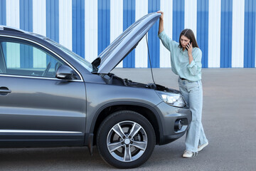 Wall Mural - Stressed woman talking on phone near broken car outdoors