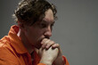 © pressmaster - Contemplative man wearing orange jumpsuit resting chin on hands, pensive expression seen on his face during serious moment of reflection