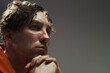 © pressmaster - Portrait of young Caucasian man resting his chin on clasped hands while looking away, appearing thoughtful and introspective with slightly disheveled hair