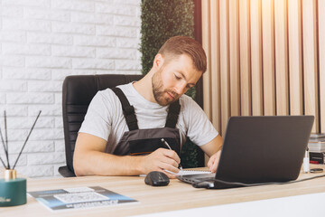 Caucasian business manager or mechanic sitting and writing report in front of laptop-notebook in office at car service