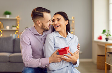 Affectionate man embracing attractive wife, girlfriend getting present from grateful husband, celebrating Valentine's Day, international women day, birthday, receiving gift wrap, happy excited family