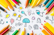 © cartoon - Overhead view of multiple colored pencils arranged on paper with cute children's drawings on the paper.