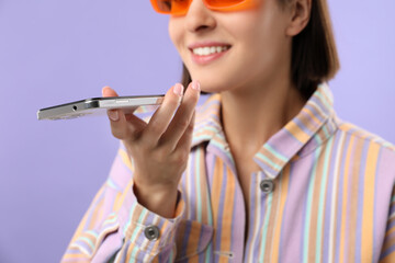 Poster - Woman in sunglasses recording voice message via smartphone on violet background, closeup