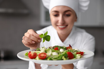 Wall Mural - Professional chef decorating delicious salad with basil in kitchen, selective focus