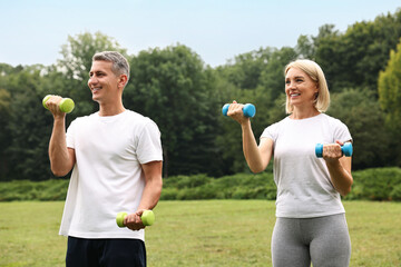 Wall Mural - Happy couple doing exercise with dumbbells in park