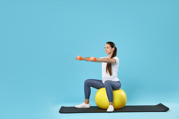 Canvas Print - Beautiful pregnant woman with dumbbells doing exercises on fitball against light blue background