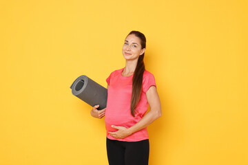 Wall Mural - Beautiful pregnant woman with exercise mat on yellow background