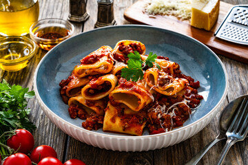 Wall Mural - Paccheri con ragù alla bolognese - noodles with bolognese sauce and grated parmesan cheese served in bowl on wooden table
