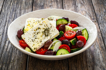 Greek style salad - fresh vegetables with feta cheese, pita bread and black olives served in bowl on wooden table
