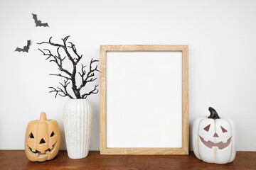 Wall Mural - Halloween mock up. Wooden frame on a wood shelf with black branches and jack o lantern decor. Portrait frame against a white wall. Copy space.