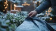 © Lamina - Hands protect snow-covered garden plants with blanket during early winter night, lights twinkling softly in the background.