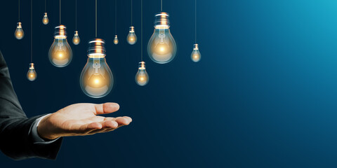 Poster - Close up of businessman hand holding glowing lamps on dark blue background with mock up place. Idea, energy, inspiration and innovation concept.