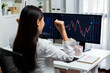 © InfiniteFlow - Successful young Asian businesswoman earning highest profit with fist up in exchange stock market on dynamic business graph on pc screens at modern office, analyzing financial technology. Stratagem.