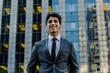 © Tanu - A young man dressed in a tailored gray suit smiles confidently as he stands outdoors in front of a contemporary office building with reflective glass.