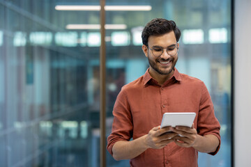 smiling programmer tests application on tablet in modern office. casual professional wears glasses a
