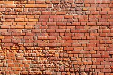 This image shows a close-up of a weathered red brick wall, highlighting its rough texture. The bricks are in a stretcher bond pattern with cracks and missing mortar, adding rustic charm.