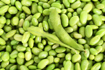 Raw green edamame pods on soybeans as background, top view