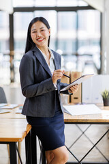 Wall Mural - Modern business asian woman in formalwear using digital tablet while standing near wooden desk in an office interior in the office. business people concept.