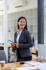 Modern business asian woman in formalwear using digital tablet while standing near wooden desk in an office interior in the office. business people concept.