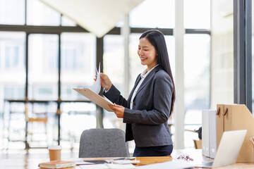 Wall Mural - Modern business asian woman in formalwear using digital tablet while standing near wooden desk in an office interior in the office. business people concept.