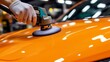 © kittikunfoto - A person wearing gloves uses a power buffer to polish the vibrant orange hood of a car, giving it a shiny, reflective finish.