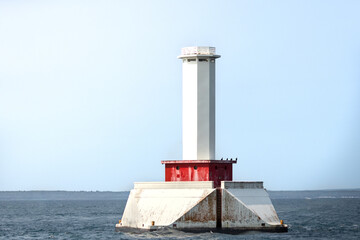 White beacon in the open water. A stalwart bright stone tower stands sentinel in the dark water of a great lake. A light house for navigation and safety for vessels on the open sea