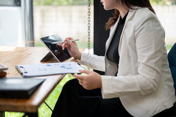 A businesswoman working on her digital tablet and paperwork at her desk in the office.