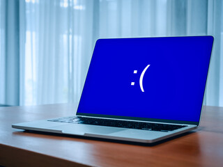 Poster - System error concept. Blue screen of death or BSOD showing, big sad emotion face, emoticon on blue display on laptop on table while problem or something went wrong on computer, in empty room.